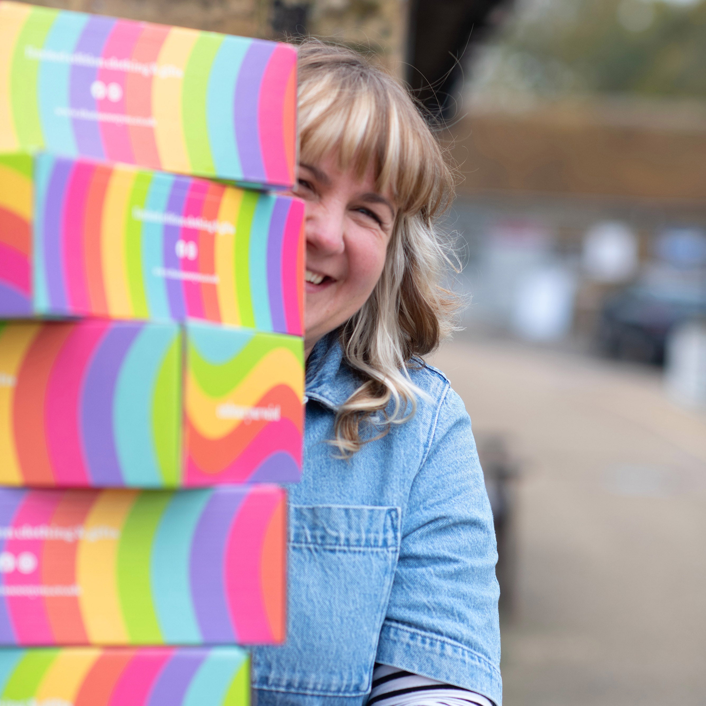 Founder, Lucy is carrying lots of That's Sooo You Rainbow gift boxes, she is wearing denim and smiling to the camera.