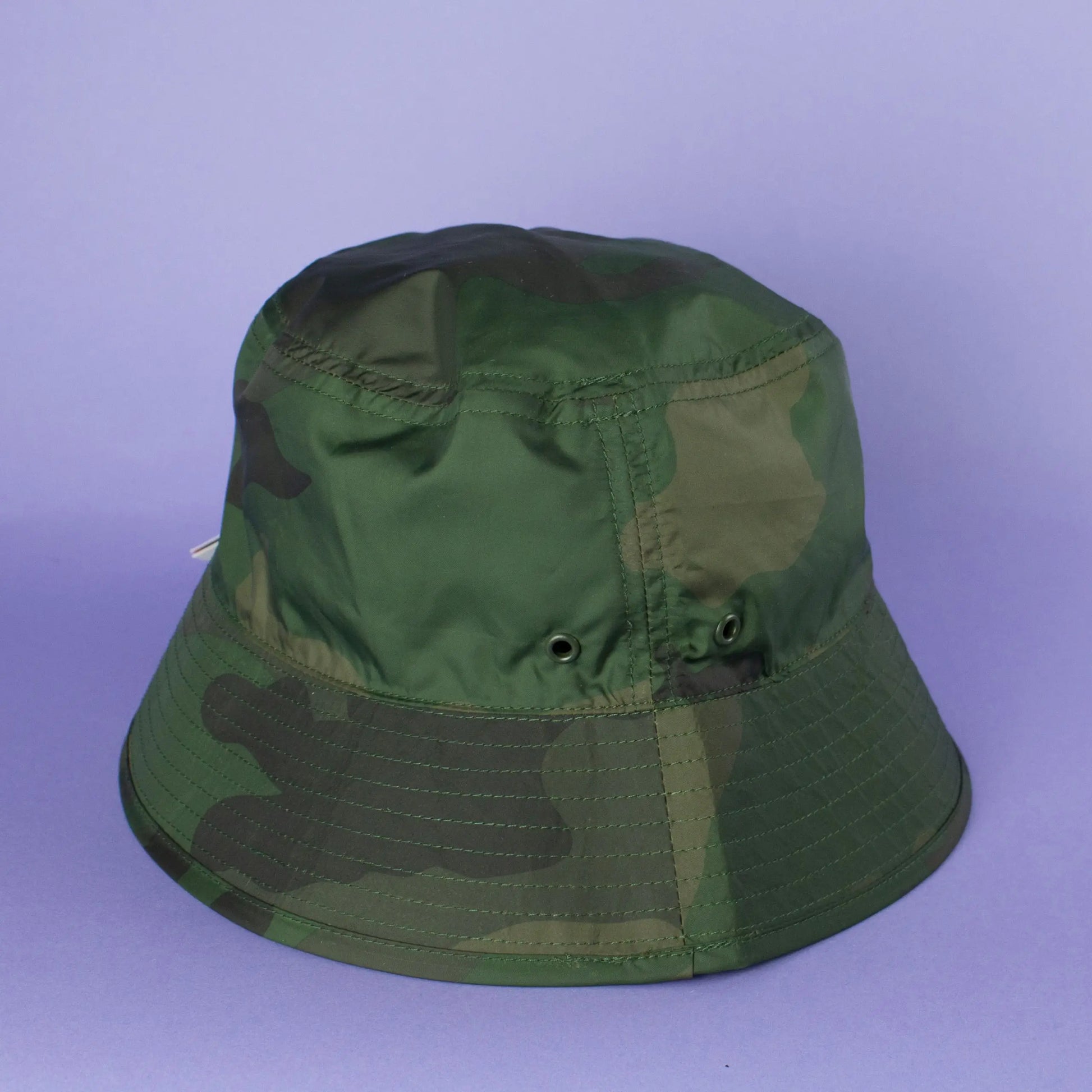 Green camouflage bucket hat with That's Sooo You hand-sewn label on it, photographed on a lilac purple background.